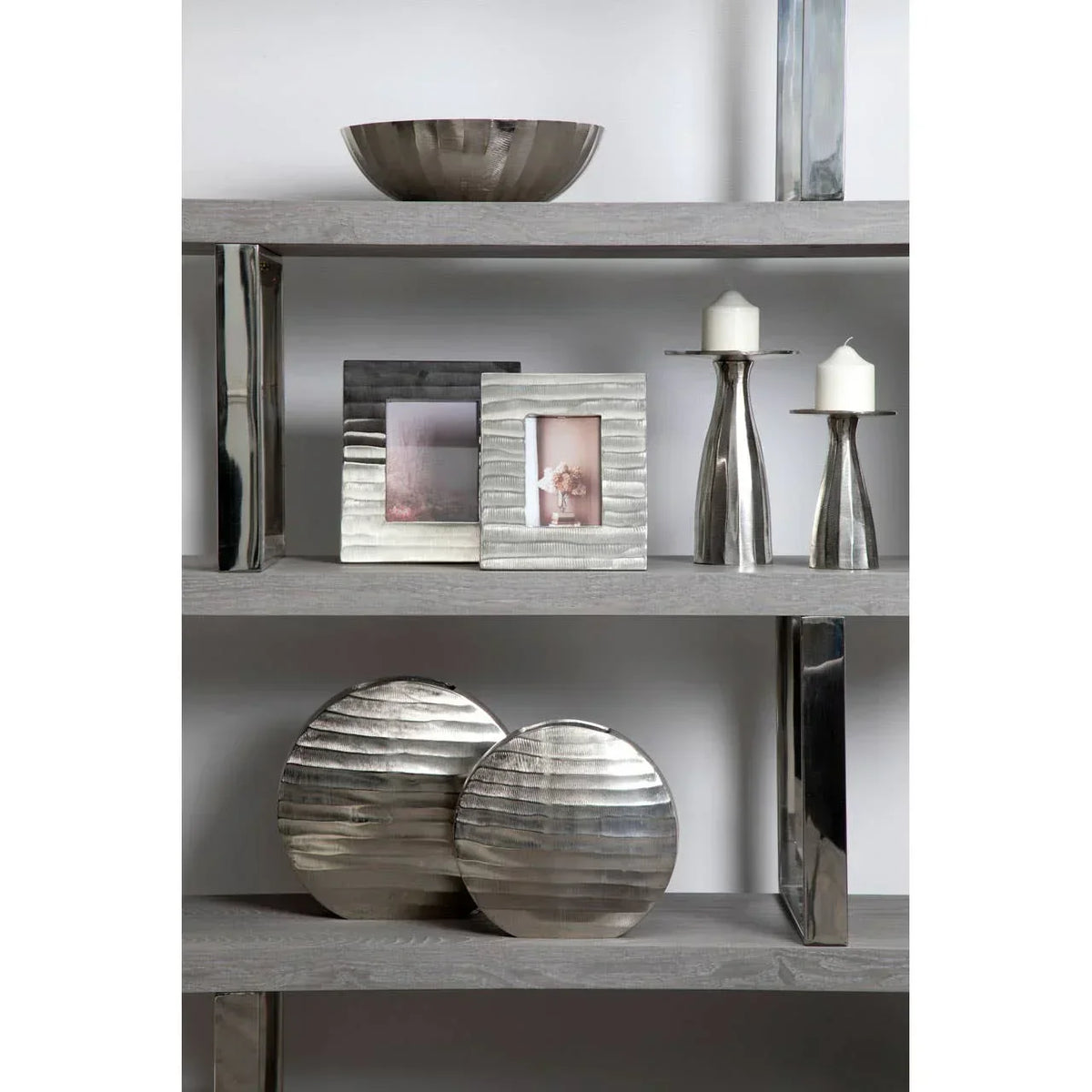 Silver metal decorative photo frames, candle holders and bowls on wooden shelving unit