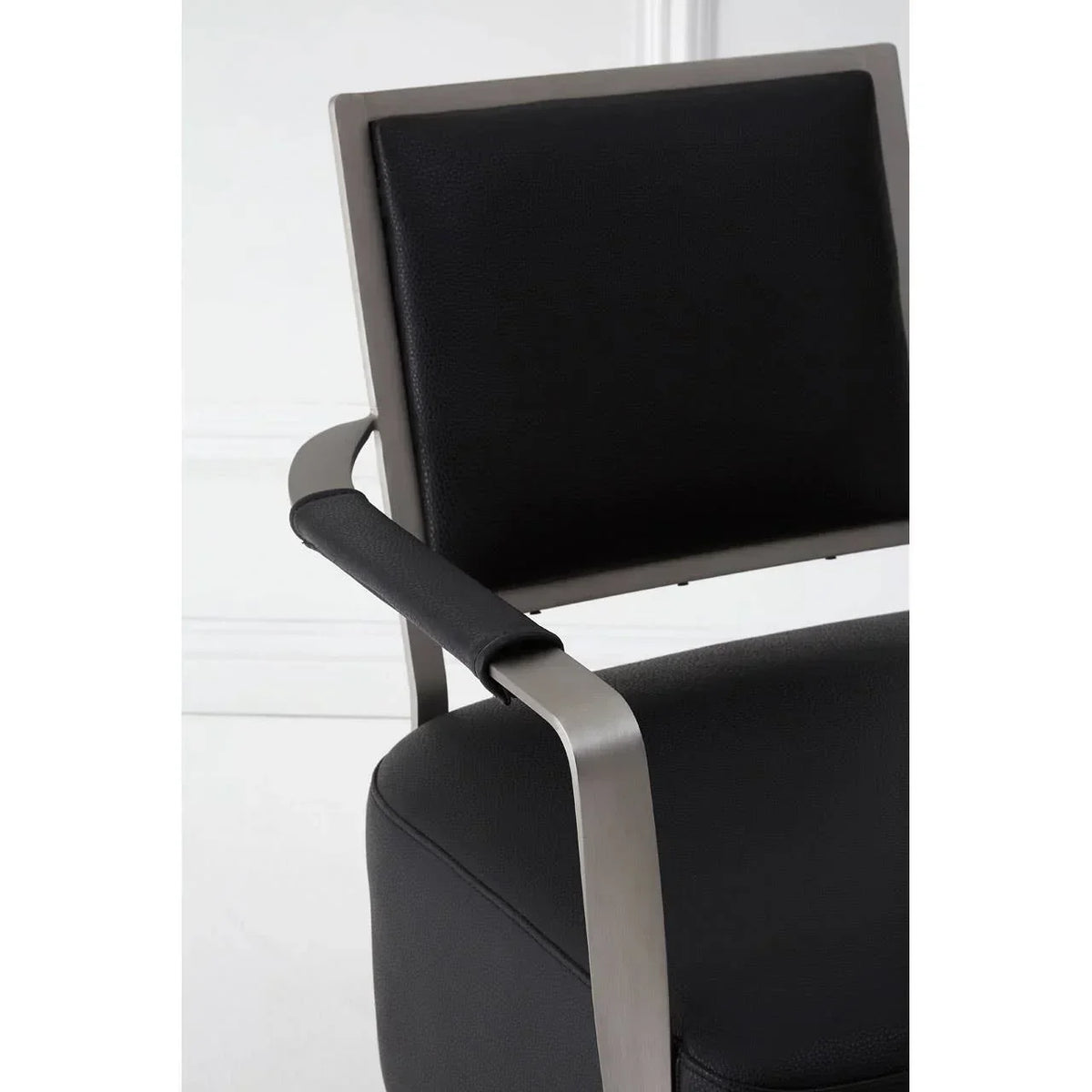 Black faux leather dining chair with brushed metal arm and cushioned backrest close-up
