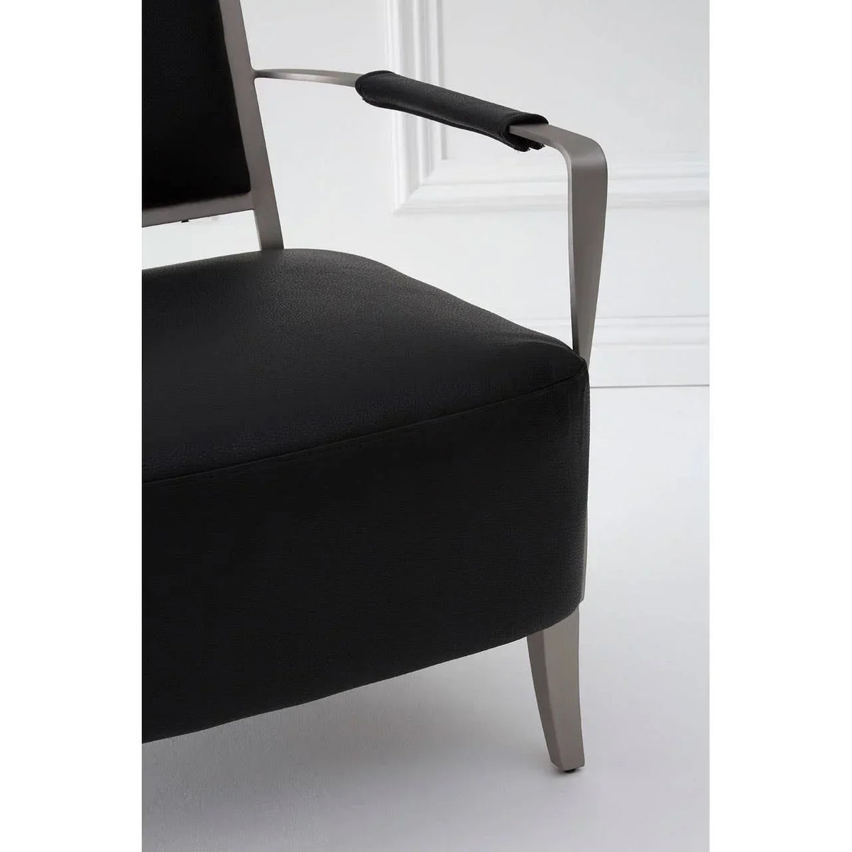 Black leather armchair with brushed metal legs and padded armrest in modern setting