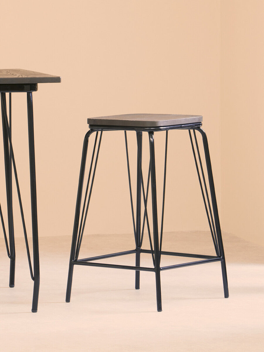 Black metal stool with a rectangular elm wood seat, featuring slender legs and a minimalist design, positioned next to a matching table against a soft beige background
