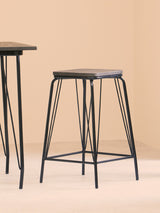 Black metal stool with a rectangular elm wood seat, featuring slender legs and a minimalist design, positioned next to a matching table against a soft beige background