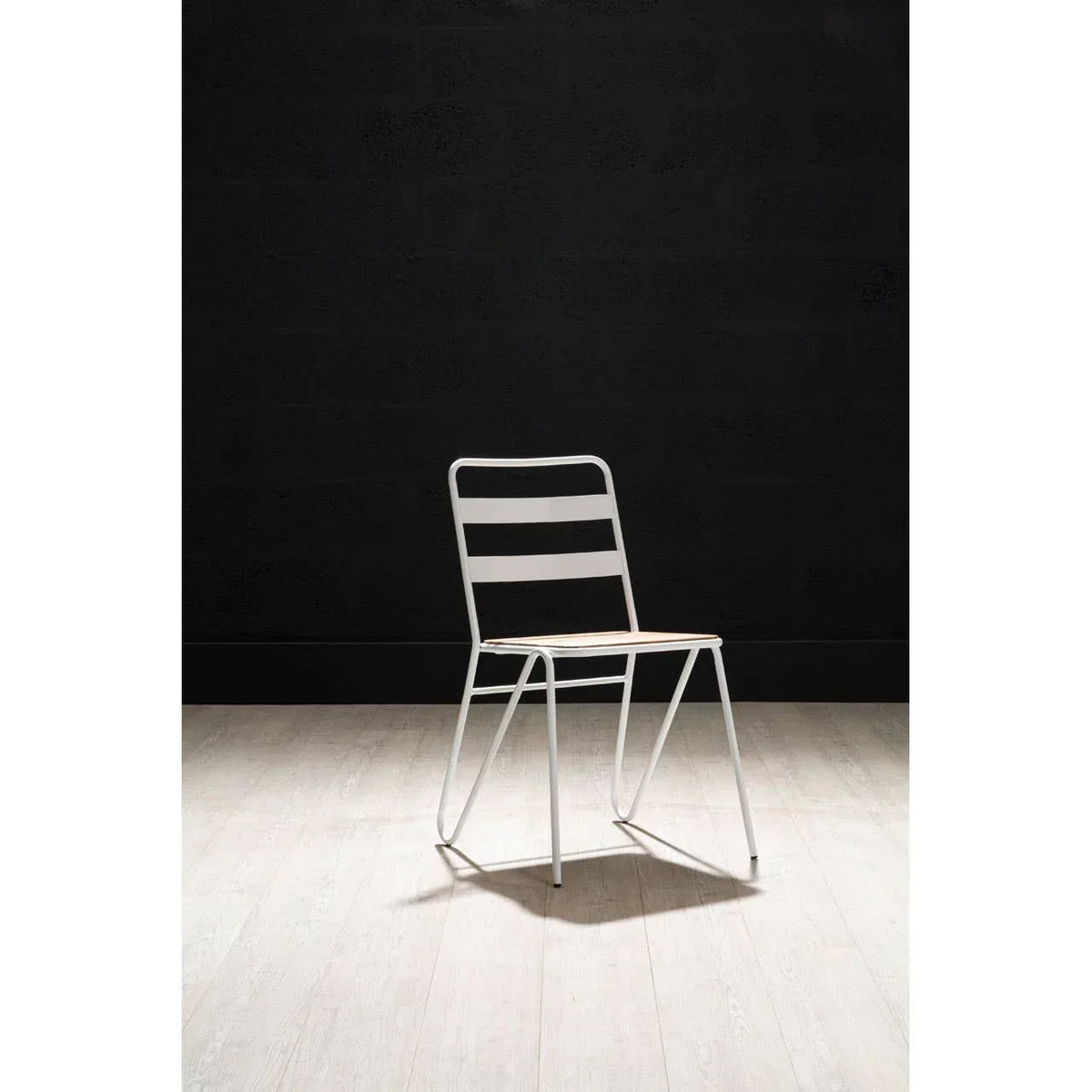 White metal dining chair with slatted backrest on light wood floor against dark wall