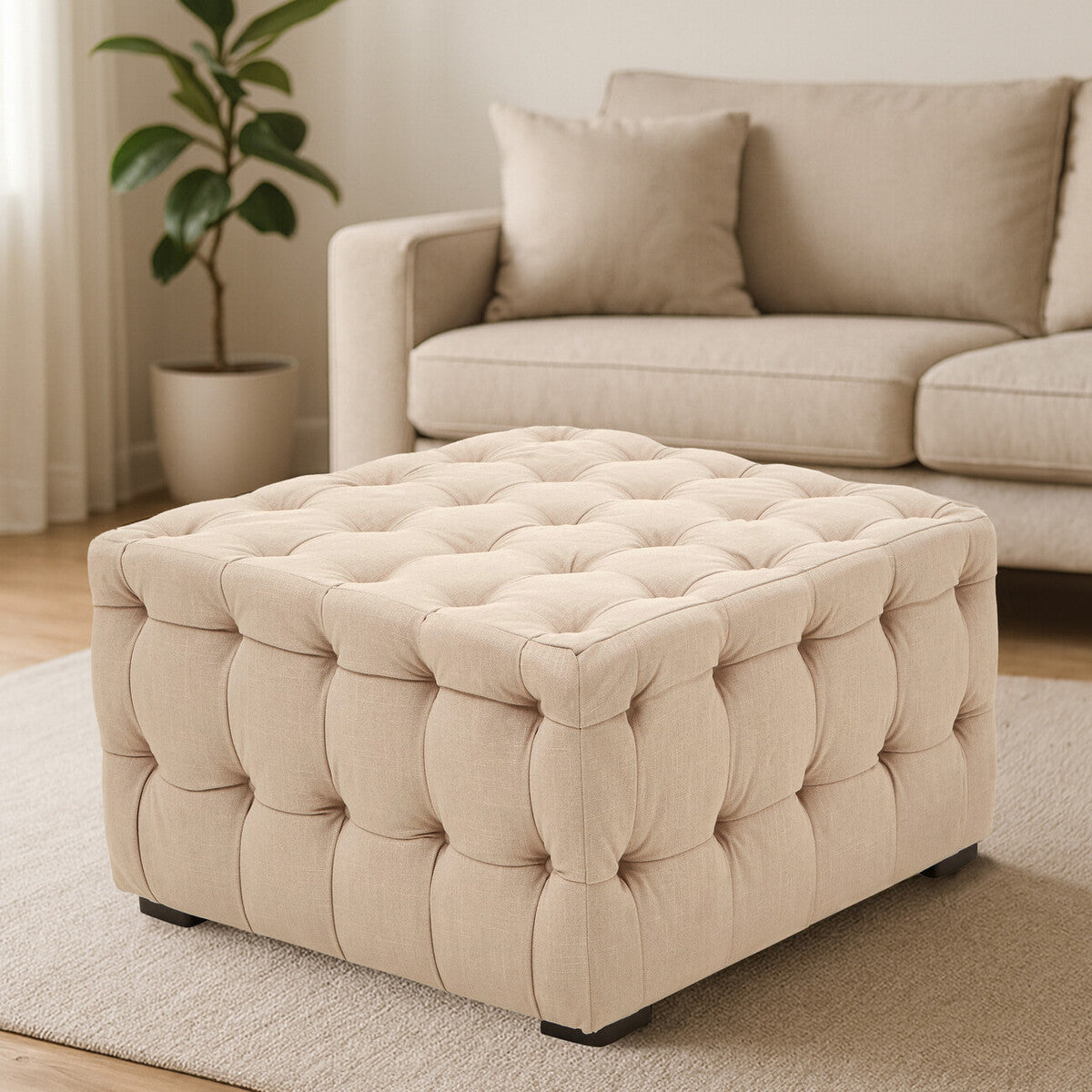 Beige linen button-tufted stool with a square shape, featuring a soft, cushioned top and decorative tufting. The stool is placed on a light-colored rug in a cozy living room setting, with a neutral-toned sofa and a potted plant in the background