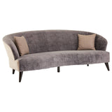A three-seat sofa upholstered in grey velvet with a curved design, featuring two beige accent pillows on either side and sleek wooden legs