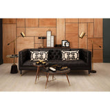 Three-seat black faux leather sofa with a modern design, featuring decorative pillows with geometric patterns. The sofa is positioned against a wooden wall, complemented by stylish floor lamps and a round coffee table with books and a decorative item on top. The flooring is light-colored wood, enhancing the contemporary aesthetic of the space