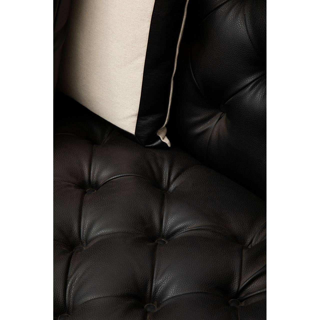 Close-up view of the tufted black faux leather upholstery of the Raven 3 Seat Sofa, showcasing the texture and stitching details along with a hint of a cream-colored cushion peeking from the side