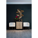A stylish bar cabinet made of mango wood featuring a gold and black finish, positioned against a dark green wall. The cabinet has multiple drawers with a sleek design, complemented by two modern white chairs on either side. Above the cabinet, there is a decorative wall art piece with a floral design. The floor is a light wood finish, enhancing the contemporary aesthetic of the space