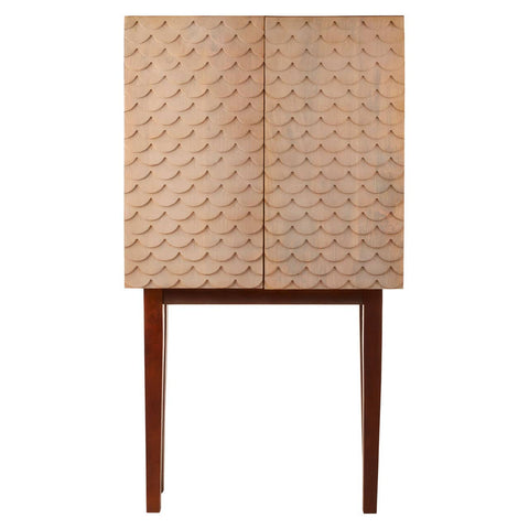 A coastal carved mango wood cabinet featuring a textured front with geometric patterns, two doors, and slender wooden legs. The cabinet has a natural wood finish that highlights the grain and craftsmanship
