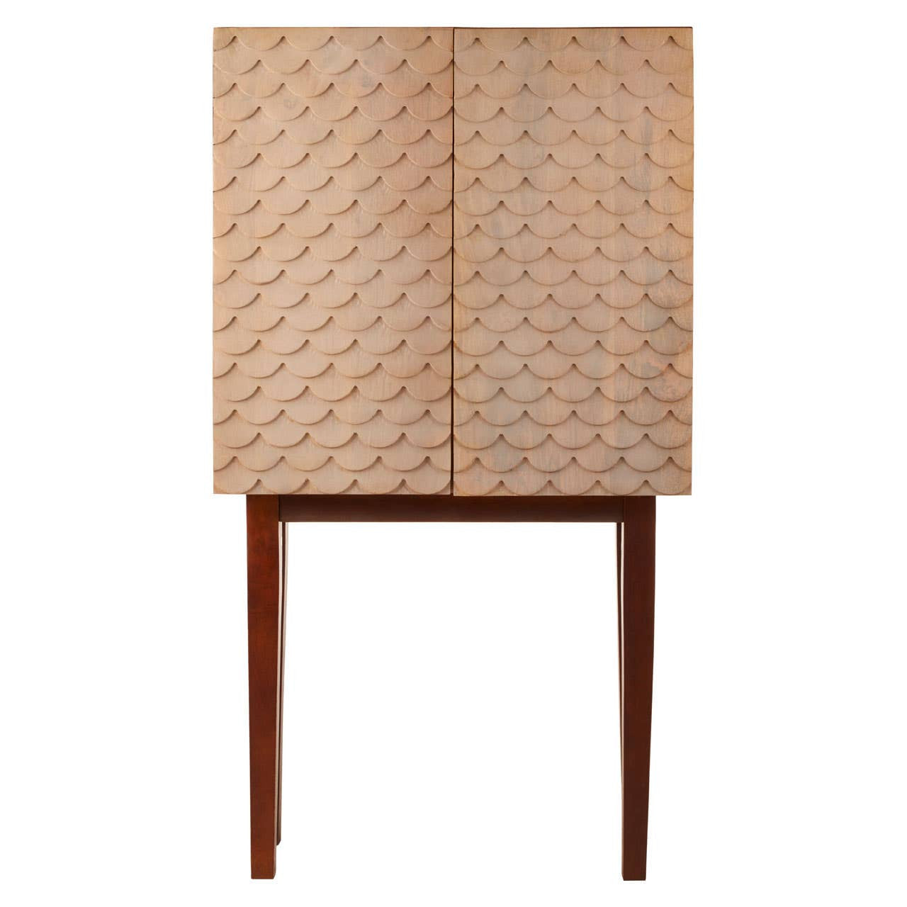 A coastal carved mango wood cabinet featuring a textured front with geometric patterns, two doors, and slender wooden legs. The cabinet has a natural wood finish that highlights the grain and craftsmanship