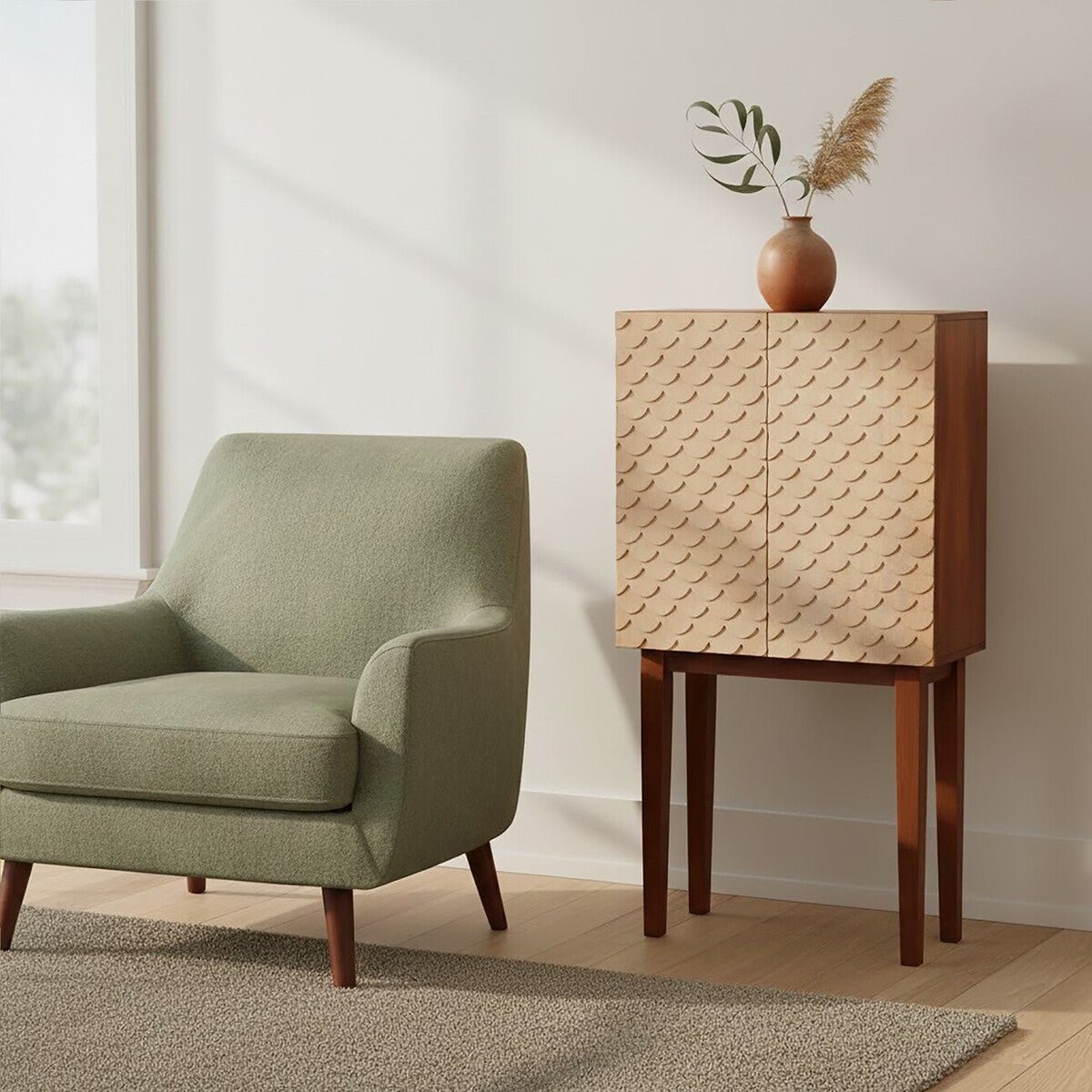 A coastal carved mango wood cabinet with a textured front design, standing on four wooden legs, next to a light green upholstered armchair. The cabinet is positioned against a wall with natural light streaming in from a nearby window, and a decorative vase with dried flowers sits on top of the cabinet. A neutral-toned rug is visible on the floor