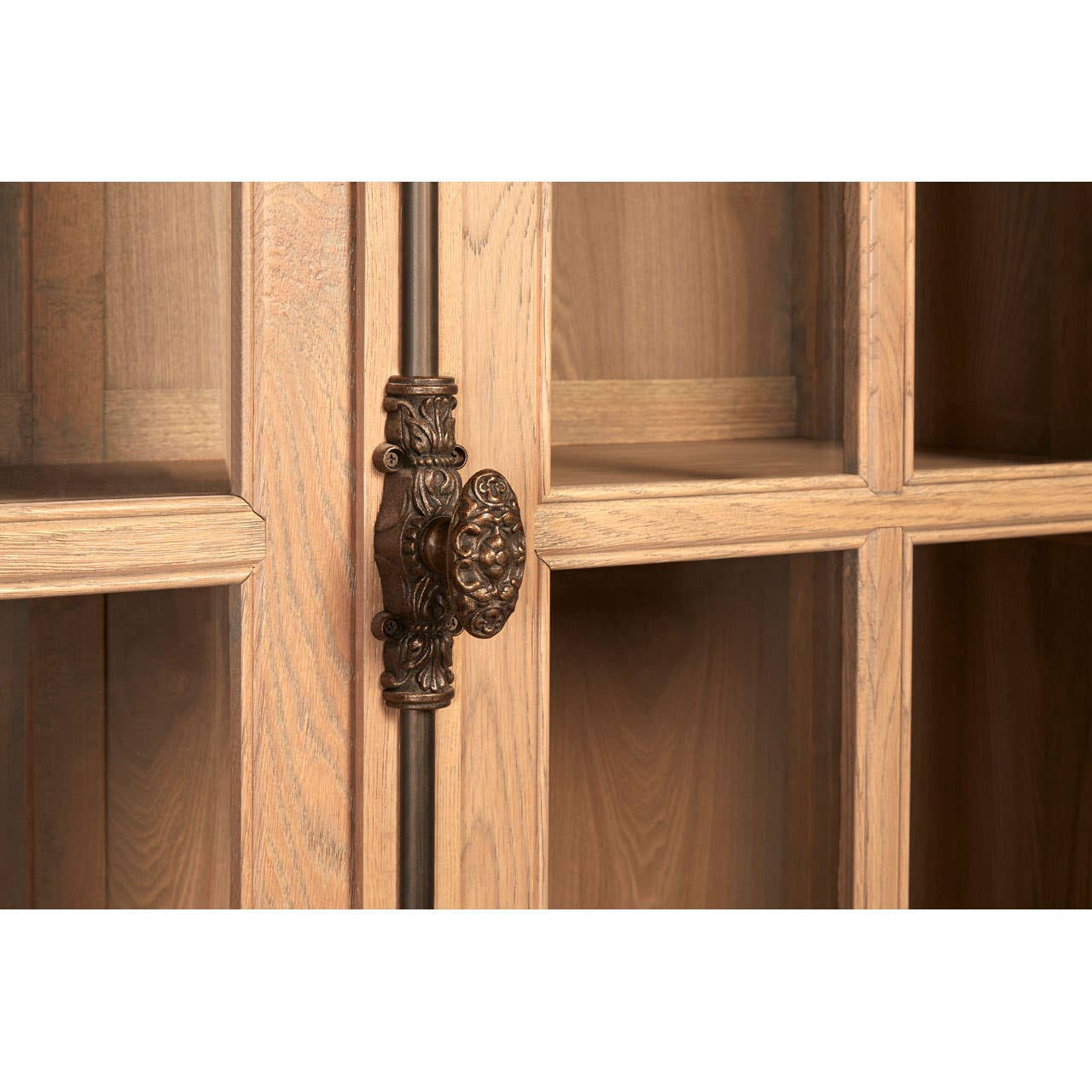 Close-up view of the Lyon Washed Grey Finish Oak Wood Tall Cabinet, highlighting the decorative metal handle and the glass-paneled doors that reveal the interior shelving. The wood has a light, washed grey finish, showcasing the natural grain and texture