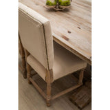 Beige upholstered dining chair with wood frame and nailhead trim at rustic dining table
