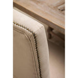 Beige upholstered dining chair with decorative brass nailhead trim and wooden table corner