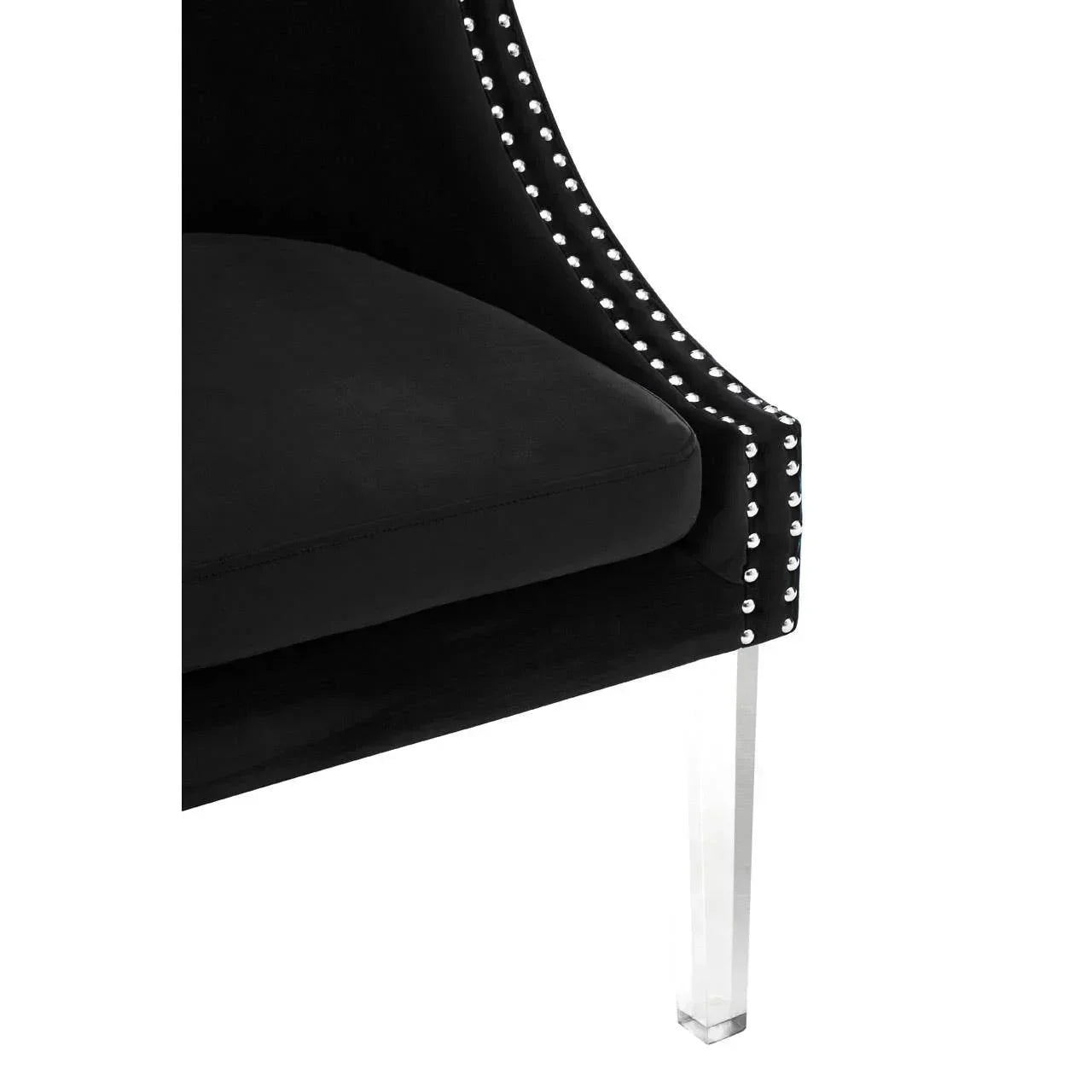 Black velvet accent chair with silver stud trim and clear acrylic leg, close-up view