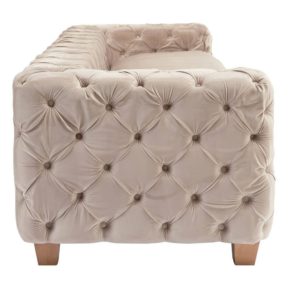 Beige velvet sofa with a tufted design, featuring a low back and armrests, supported by light wooden legs. The fabric has a soft, luxurious appearance, highlighting its elegant style suitable for home decor