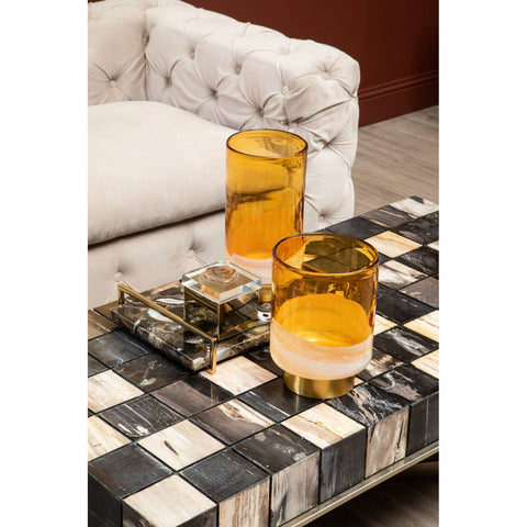 Beige velvet sofa with three seats featuring tufted detailing, positioned next to a stylish coffee table. The coffee table has a black and white patterned surface adorned with two amber-colored glasses and a decorative tray. The background includes a warm-toned wall, enhancing the cozy atmosphere