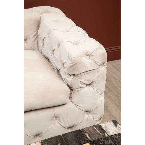 Beige velvet sofa with a tufted design, featuring a plush armrest and soft upholstery, set against a warm-toned wall. The sofa's elegant texture and color create a cozy and inviting atmosphere