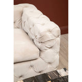Beige velvet sofa with a tufted design, featuring a plush armrest and soft upholstery, set against a warm-toned wall. The sofa's elegant texture and color create a cozy and inviting atmosphere