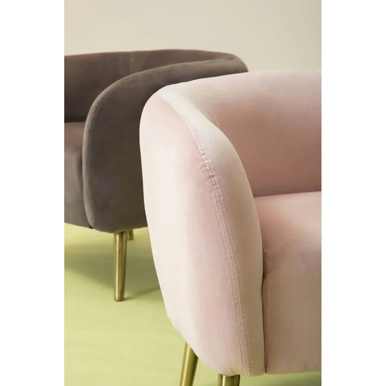 Blush pink velvet armchair with gold legs and curved armrest, brown velvet chair behind