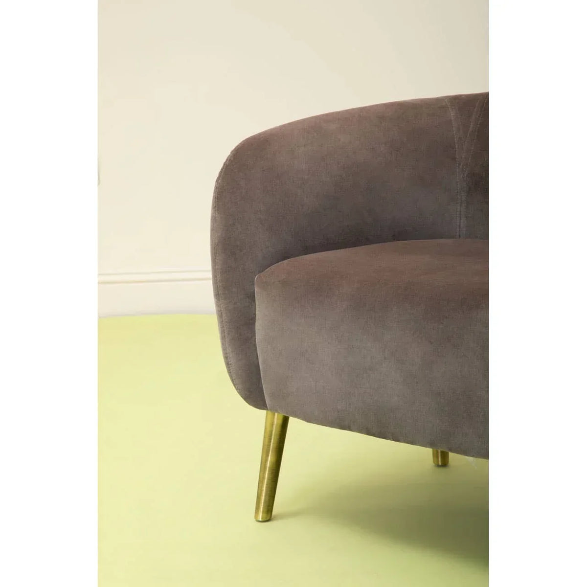 Grey velvet sofa with curved armrest and gold metal legs, close-up side view
