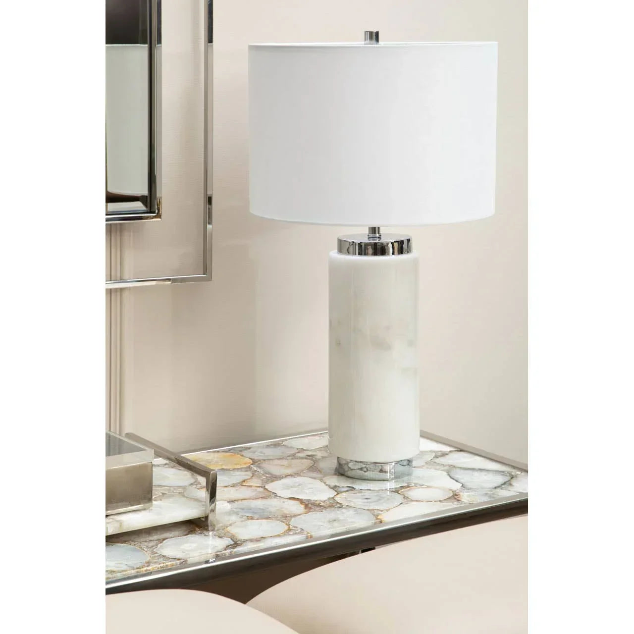 White marble table lamp with cylindrical base and chrome detail on stone side table