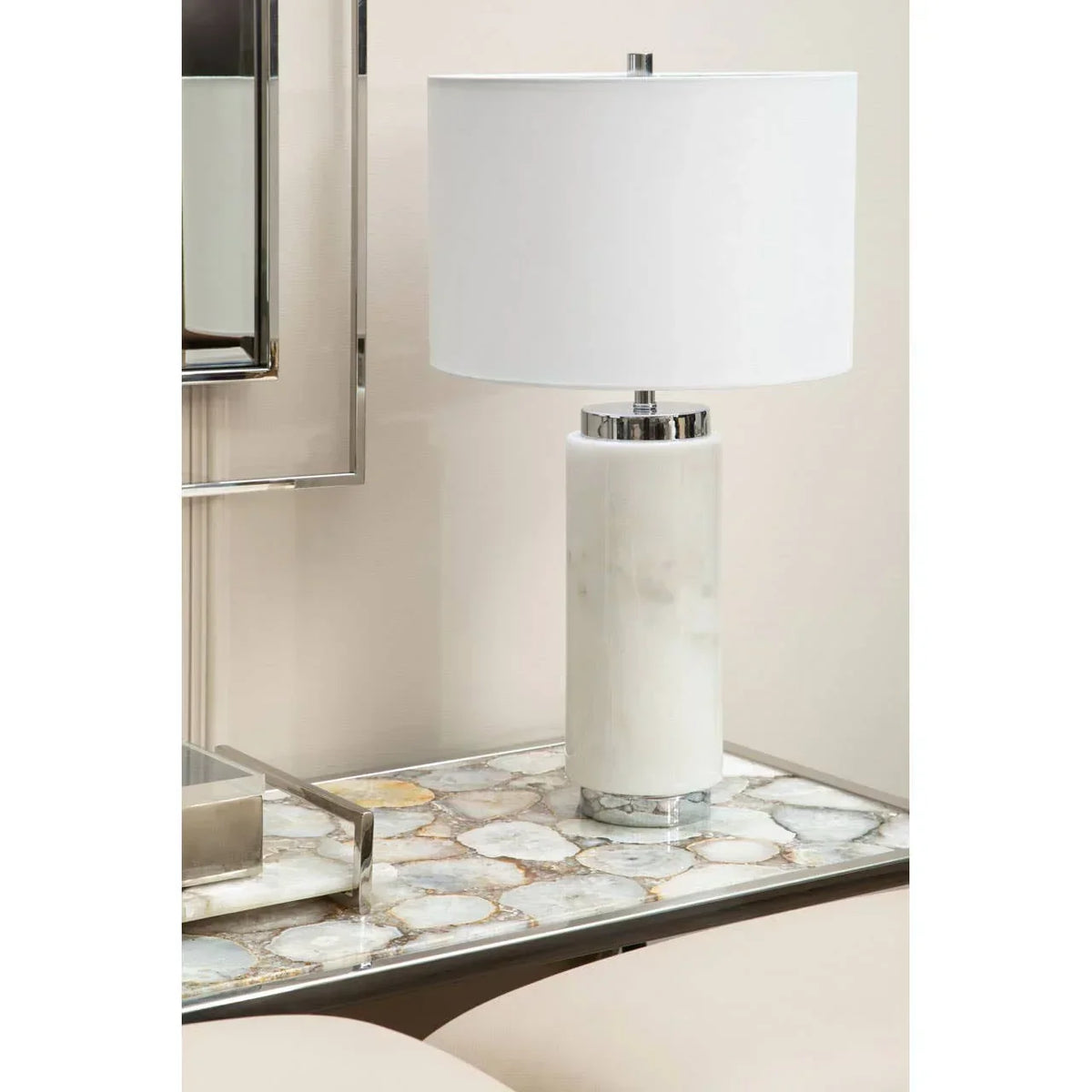 White marble table lamp with cylindrical base and chrome detail on stone side table