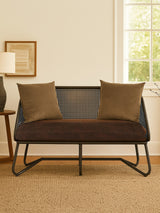 A two-seat sofa with a sleek design featuring curved legs, upholstered in a dark fabric. The sofa is adorned with two square, textured throw pillows in a complementary color. It is positioned in a cozy room with natural light coming through a window, and a light-colored rug is visible beneath it. A lamp and framed artwork are in the background, adding to the inviting atmosphere