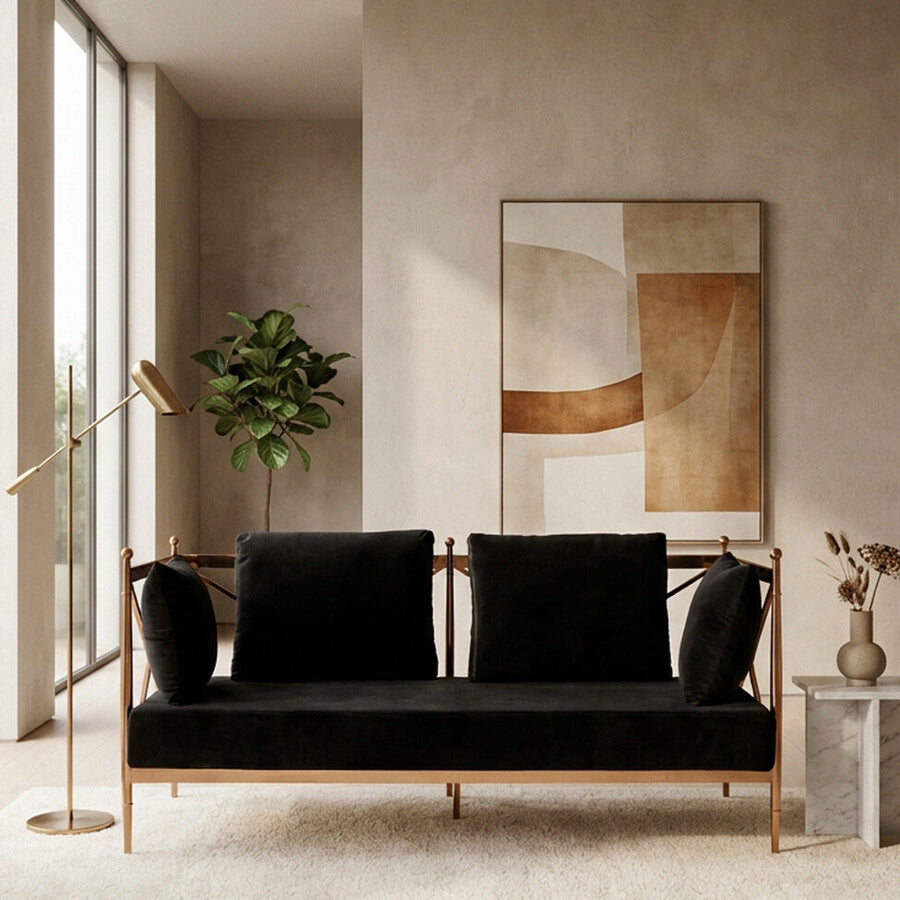 A stylish two-seater sofa featuring a black velvet upholstery and a rose gold metal frame, positioned in a modern living space with large windows, a potted plant, and a decorative vase on a light-colored rug. A large mirror is mounted on the wall behind the sofa, reflecting the room's contemporary design elements