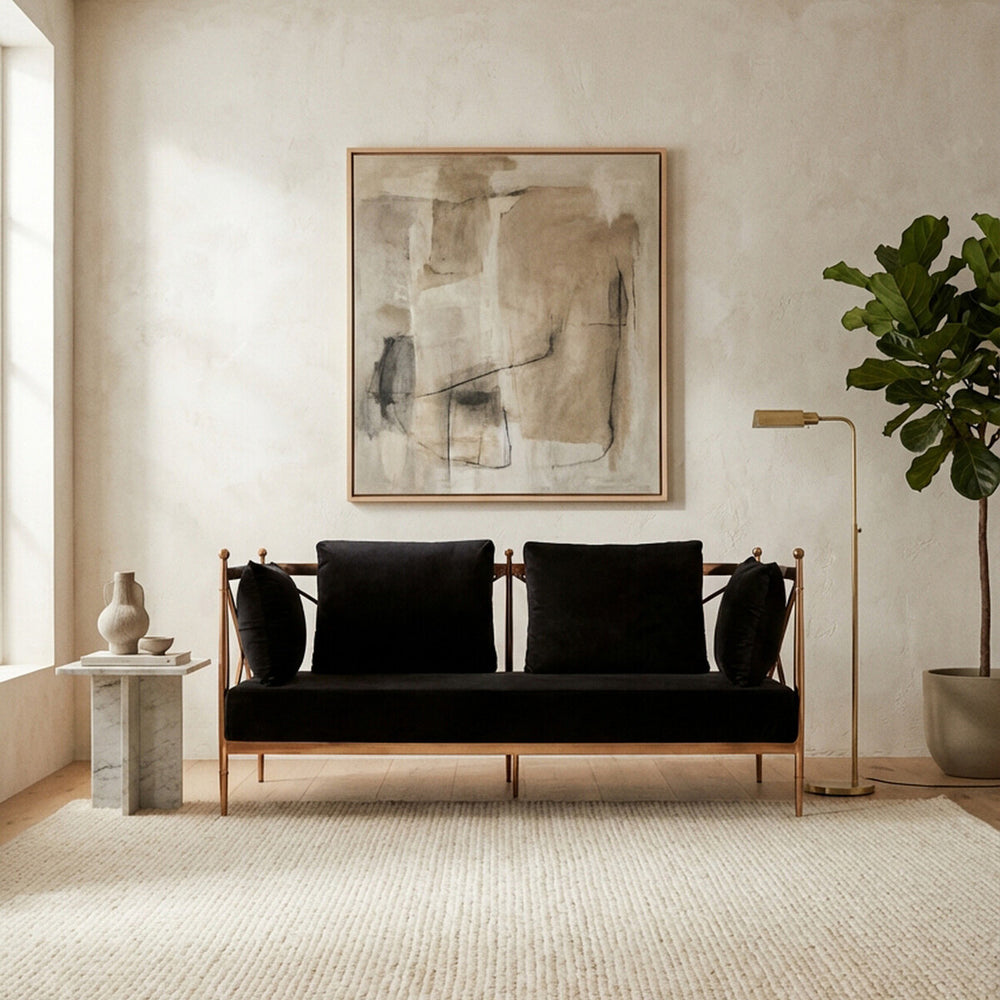 A two-seater sofa featuring a sleek black velvet upholstery and a stylish rose gold frame, positioned in a bright room with a large abstract artwork on the wall. The sofa is complemented by two black cushions and is set against a light-colored carpet, with a potted plant and a floor lamp visible in the background