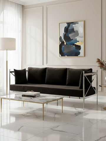 A sleek three-seater sofa upholstered in black velvet, featuring a modern silver frame. The sofa is positioned in a bright room with large windows, complemented by a minimalist coffee table and an abstract artwork on the wall. Soft natural light enhances the elegant design and luxurious texture of the fabric