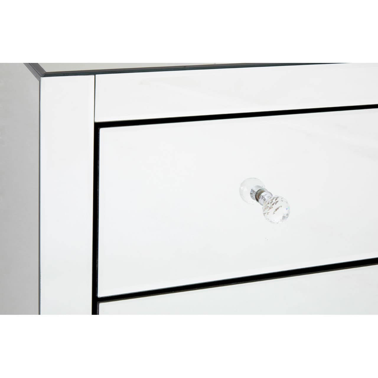 A close-up view of the Graciela Chest of 4 Drawers, featuring a sleek white finish with a subtle black outline around the drawers. Each drawer has a simple, elegant silver knob for easy access. The surface is smooth and reflective, enhancing the modern aesthetic of the furniture piece