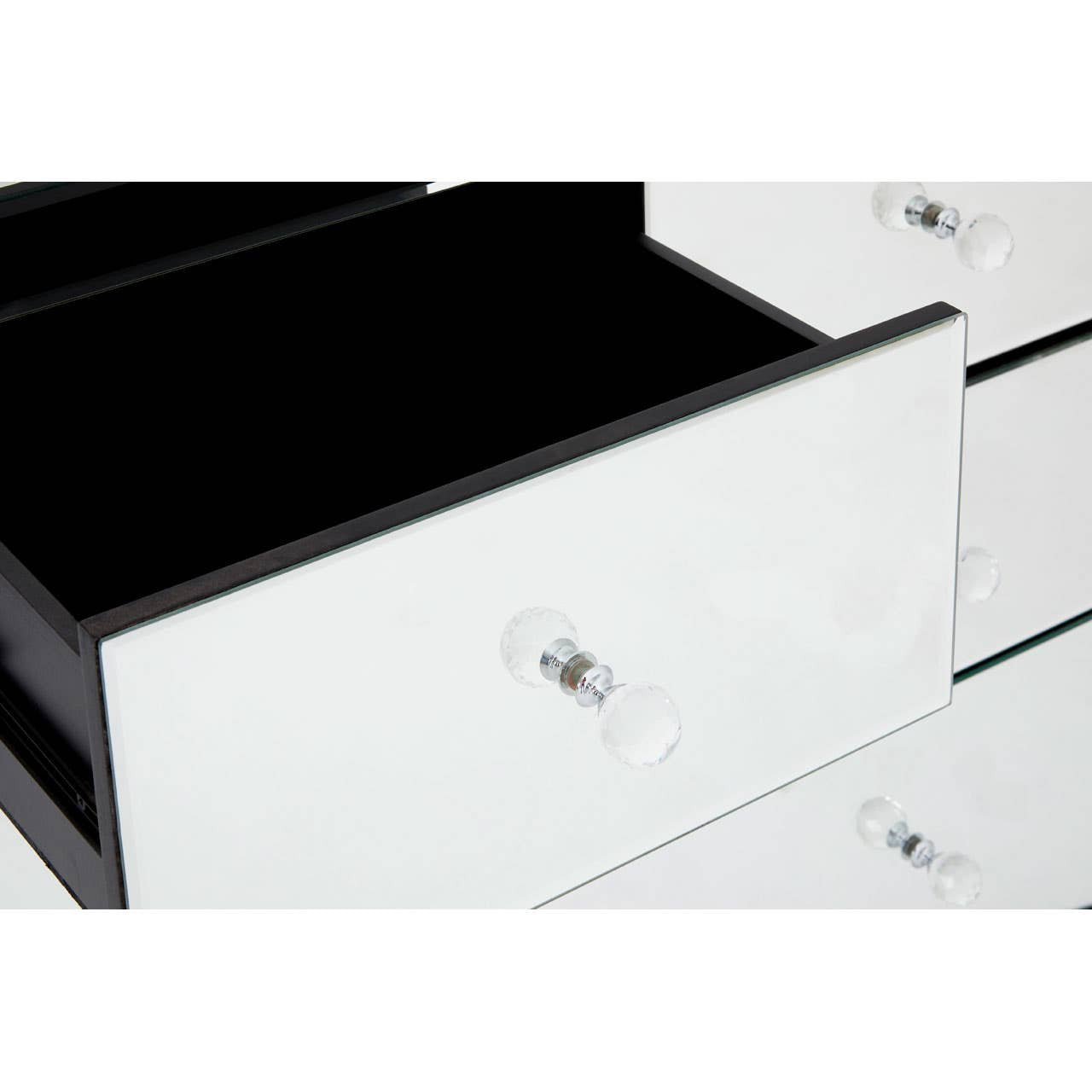 A close-up view of a white drawer from the Graciela Chest of 4 Drawers, featuring a sleek design with a shiny surface and a crystal-like knob. The drawer is partially open, revealing a black interior. The surrounding drawers are also visible, showcasing the modern aesthetic of the furniture piece