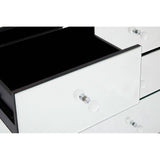 A close-up view of a white drawer from the Graciela Chest of 4 Drawers, featuring a sleek design with a shiny surface and a crystal-like knob. The drawer is partially open, revealing a black interior. The surrounding drawers are also visible, showcasing the modern aesthetic of the furniture piece