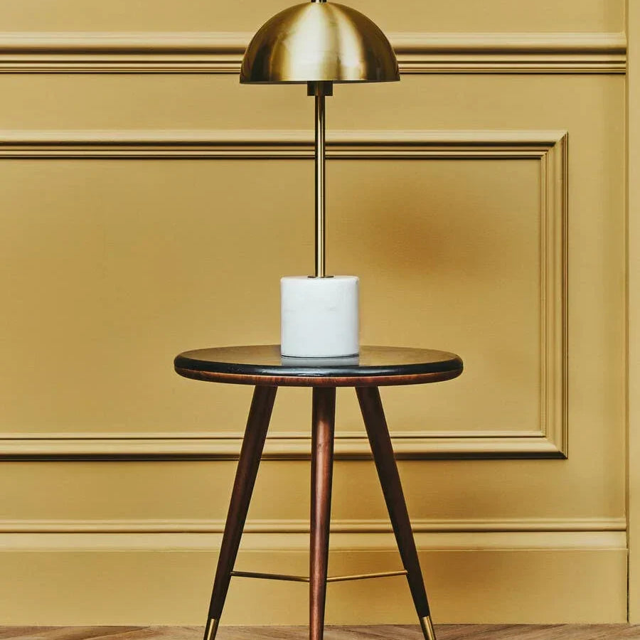 Round wooden side table with gold floor lamp and marble base against yellow panel wall
