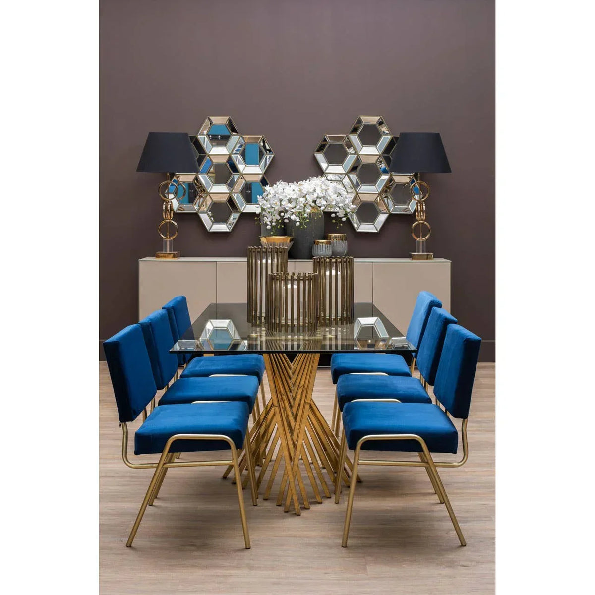 Glass dining table with gold legs and six blue velvet chairs in modern dining room