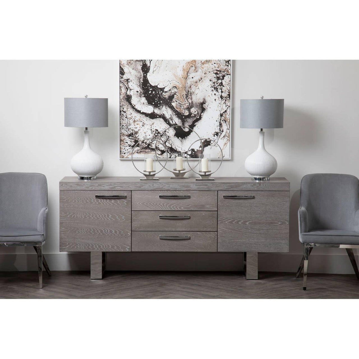 Grey sideboard with drawers and cabinets, flanked by chairs, topped with lamps and decor
