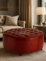 Round button tufted stool in antique brown leather, featuring a plush top with deep button detailing and a smooth, rounded base. The stool is positioned in a cozy living room setting, with a soft rug beneath it and a warm lamp in the background, creating an inviting atmosphere