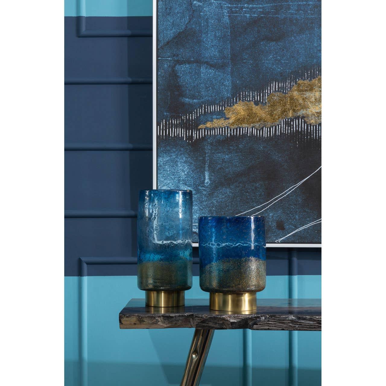 Pair of blue glass vases with gold bases on dark wood console table against blue wall art