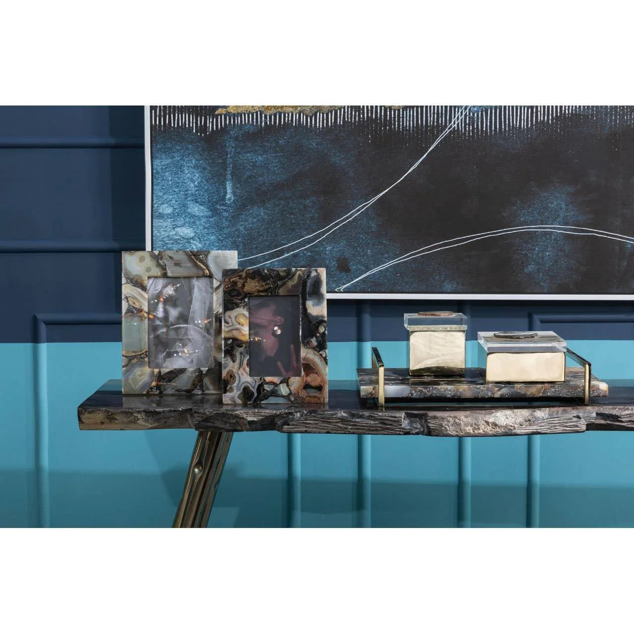 Agate photo frames and decorative boxes on console table against blue paneled wall