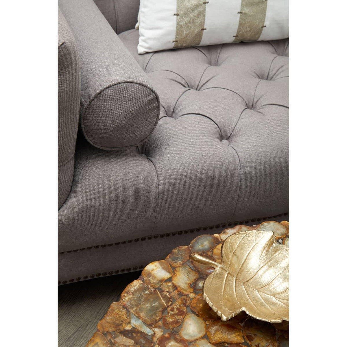 Grey tufted sofa with bolster armrest beside marble coffee table and decorative gold leaf dish