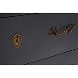 Close-up of black chest of drawers with ornate brass handle and keyhole
