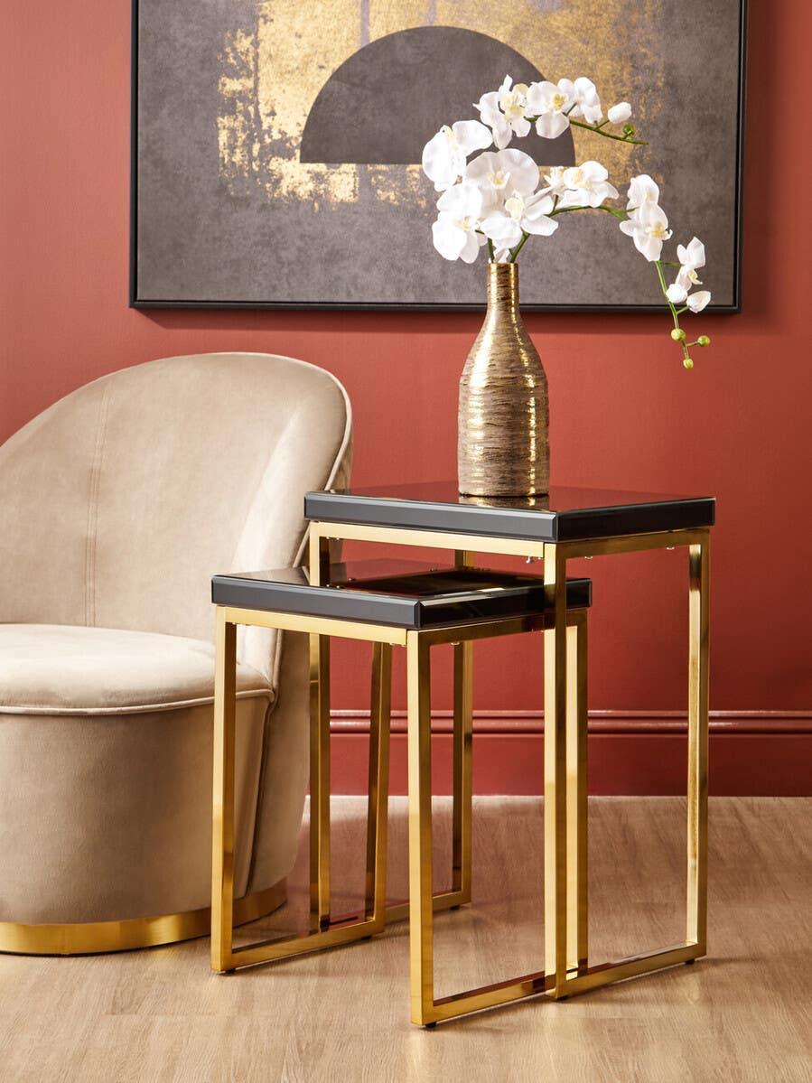 Gold metal and black glass nesting tables beside beige accent chair in modern living room