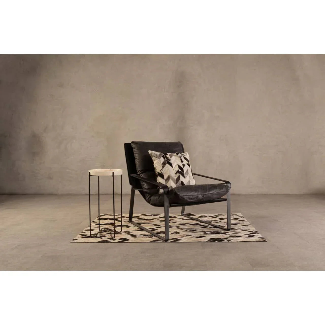 Black leather accent chair with geometric cushion beside marble top side table on patterned rug