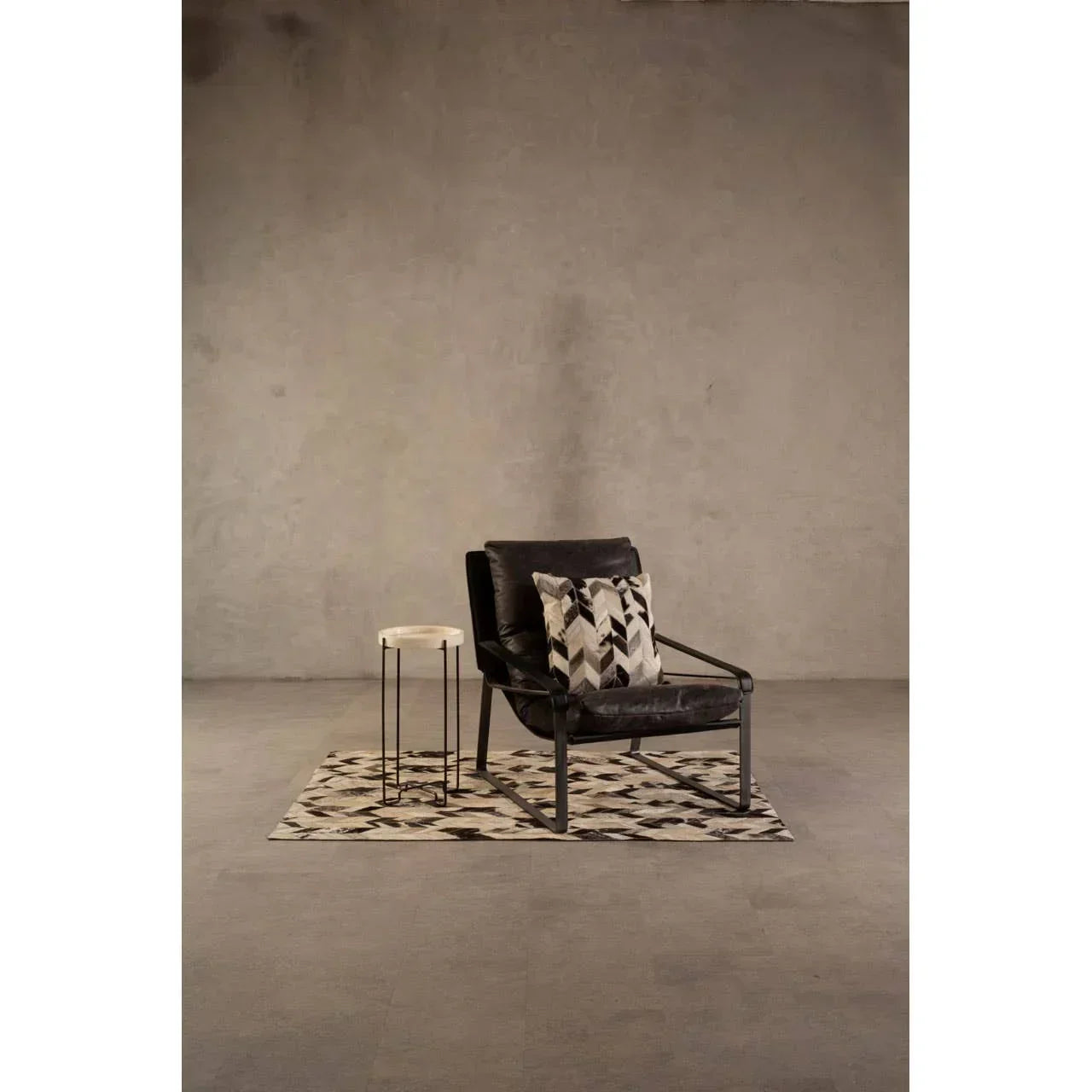 Black leather accent chair with patterned cushions beside round side table on geometric rug
