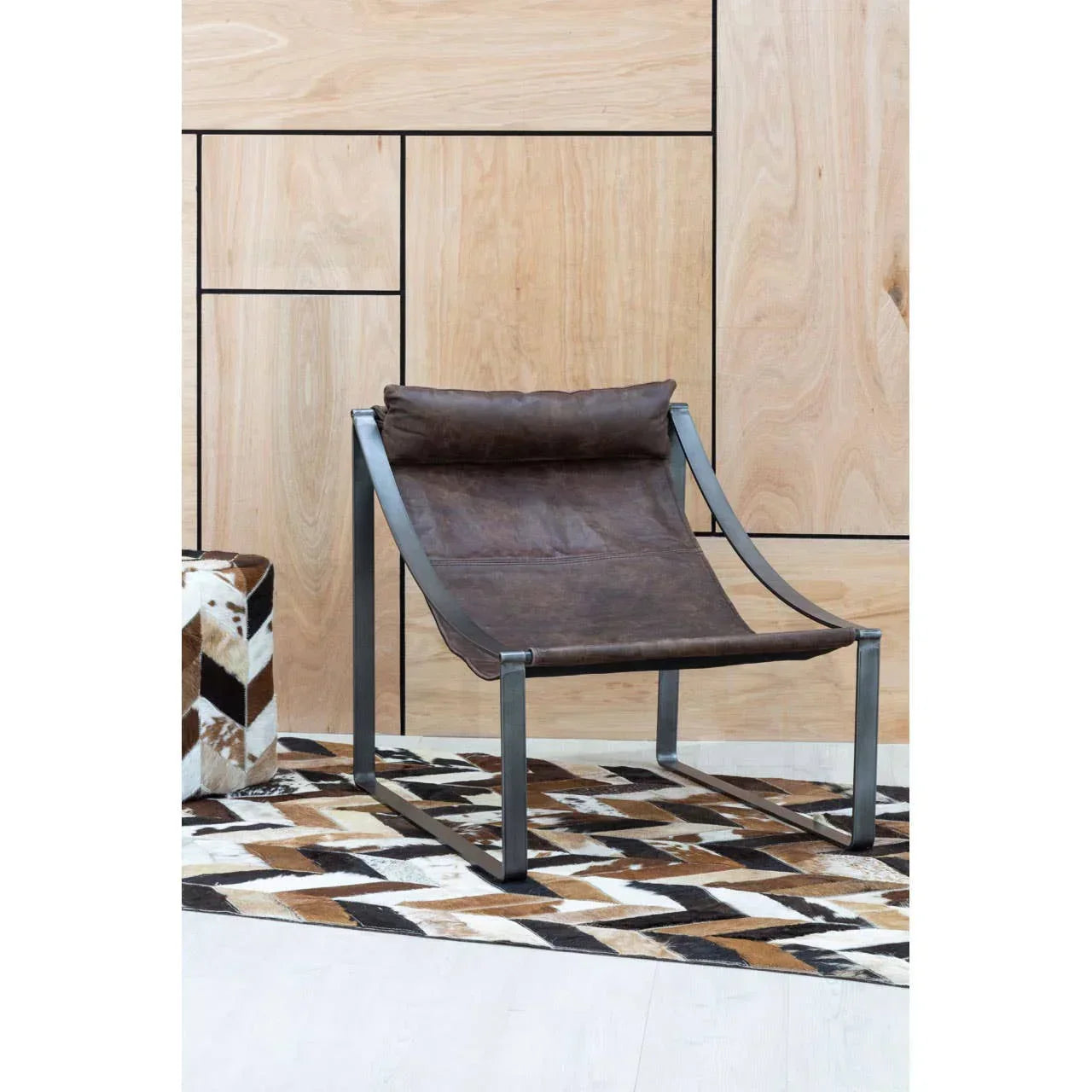 Brown leather lounge chair with metal frame on geometric rug against wood panel wall