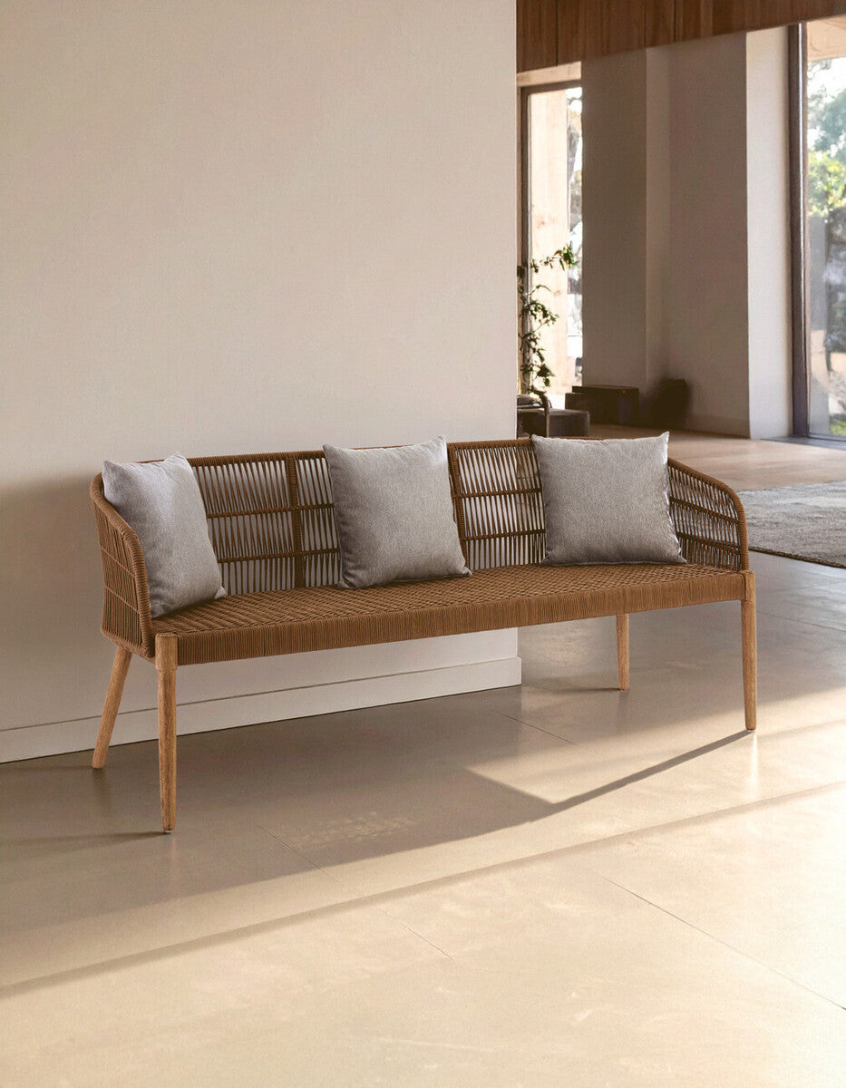 Three-seater sofa featuring a woven rope design with a wooden frame, complemented by three light gray cushions. The sofa is positioned against a neutral wall in a well-lit room with large windows, showcasing a modern and minimalist aesthetic