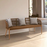 A three-seater sofa featuring a woven rope design with a wooden frame and legs. The sofa is adorned with three light gray cushions, positioned against a neutral wall in a bright, airy room with natural light streaming in. The floor is a light-colored material, enhancing the modern aesthetic of the space