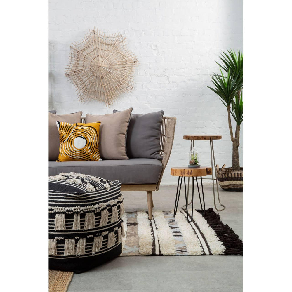 Modern grey sofa with textured cushions, round pouffe, striped rug, and nesting side tables