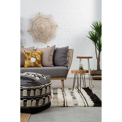 Modern grey sofa with textured cushions, round pouffe, striped rug, and nesting side tables