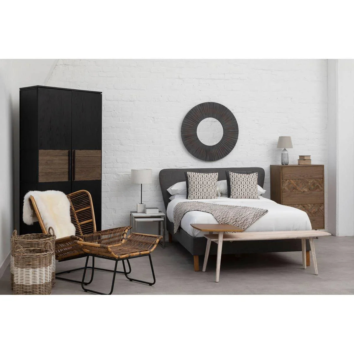 Modern bedroom with grey upholstered bed, geometric cushions, rattan chair, wooden wardrobe